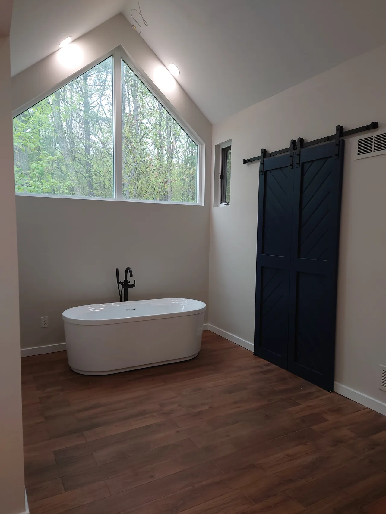 Freestanding tub beneath a vaulted window beside dark sliding doors