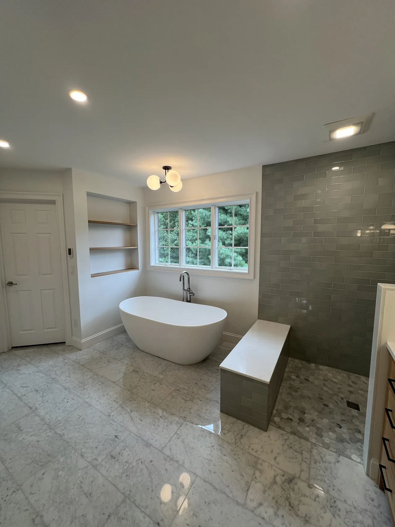 Modern bathroom with a freestanding tub, blue-gray shower tile, and wood accents